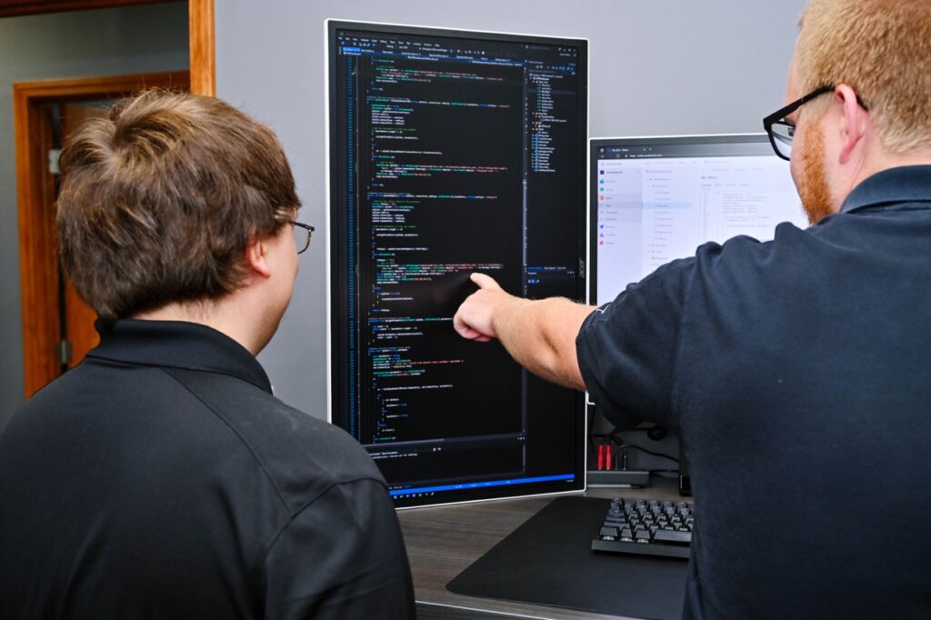 Justin white pointing to aspect of code next to another employee