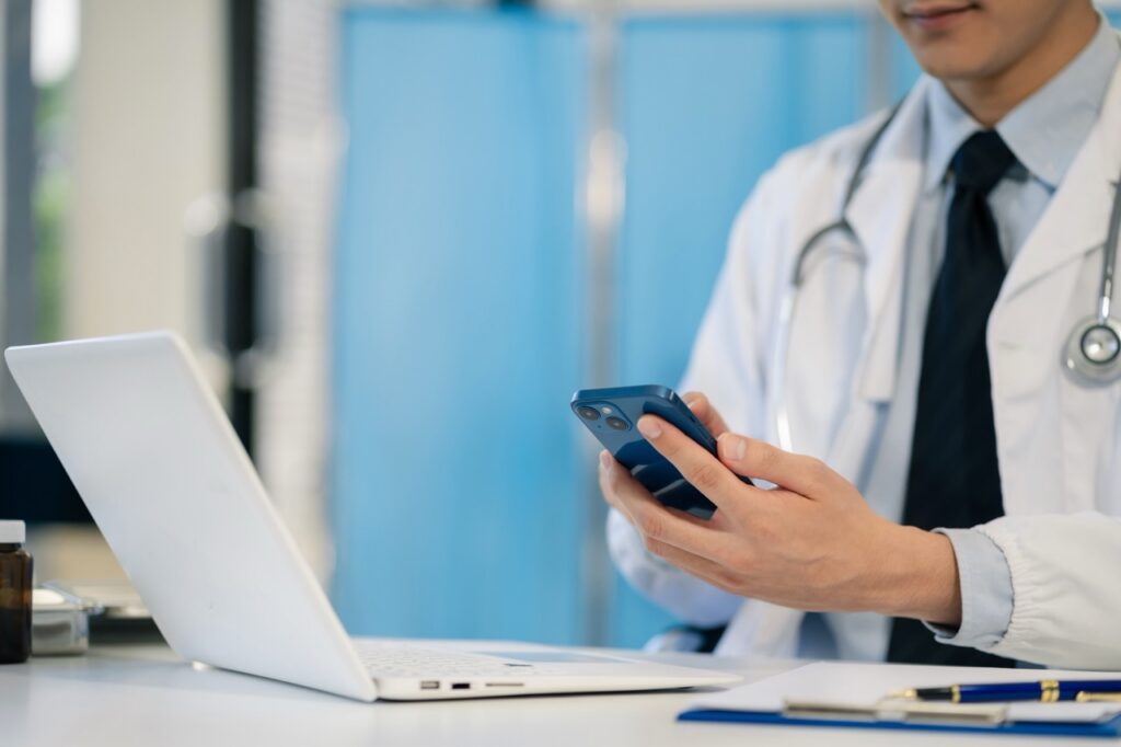 Doctor holding iphone sitting in front of laptop